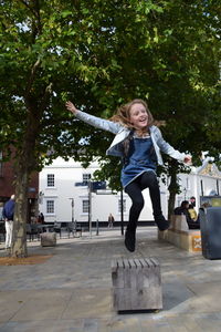 Full length of smiling young woman jumping against trees