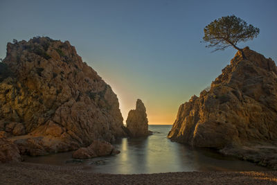 Rock formations by sea against clear sky