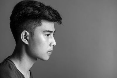 Profile view of young man looking away against gray background