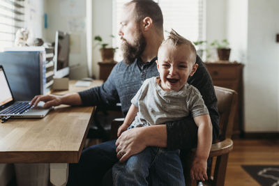 Father trying to work from home with toddler screaming in his lap