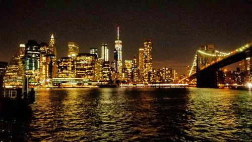 Illuminated city by sea against sky at night