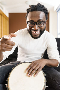 Portrait of smiling young man playing tambourine at home
