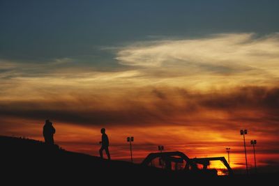 Silhouette people on land against orange sky during sunset