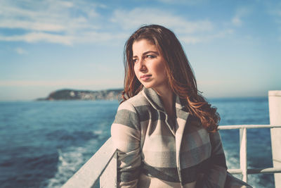 Portrait of young woman standing by railing against sea