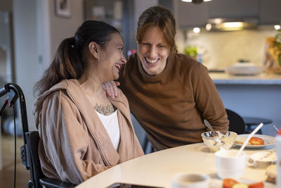 Happy caregiver and woman with paraplegia talking to each other at home