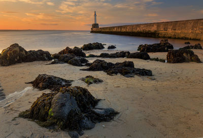 Calm evening view of rocky beach with harbour pier in background