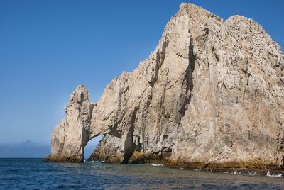 Rock formations in sea against clear blue sky