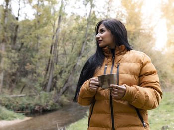 Young woman looking away while standing against trees
