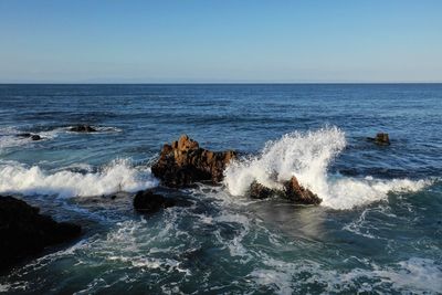 Waves splashing on rocks in sea against blue sky