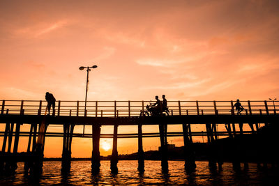 Silhouette people on pier over sea against sky during sunset