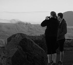 Rear view of man photographing woman standing on rock