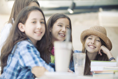 Portrait of smiling teenage friends with books sitting on desk