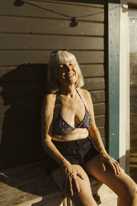 Portrait of young woman sitting on wooden wall