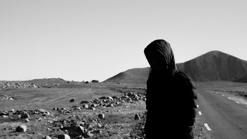 Man wearing hooded jacket while standing against sky at desert