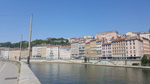 Buildings by river against clear blue sky