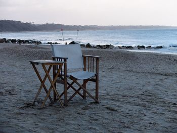 Chairs on table by sea against sky