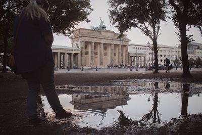 Reflection of woman standing on puddle in city