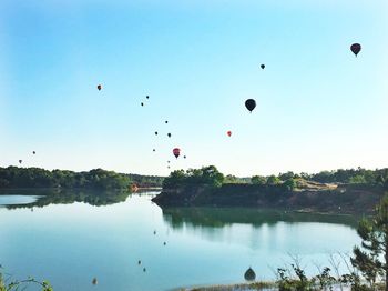 Hot air balloons flying over lake against clear sky