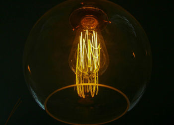 Close-up of illuminated light bulb hanging against black background