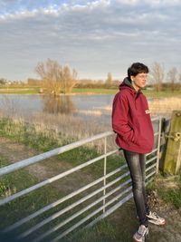 Full length of boy standing by railing against sky