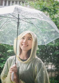 Smiling young woman holding umbrella during rainfall