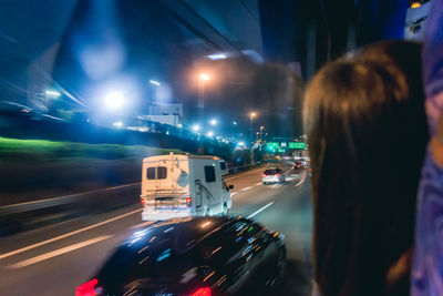 Woman looking vehicles on street through bus window at night