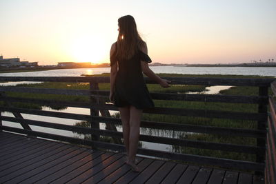 Woman standing on railing against sea during sunset