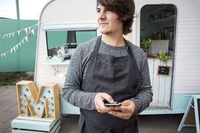 Thoughtful male owner holding smart phone while standing against food truck