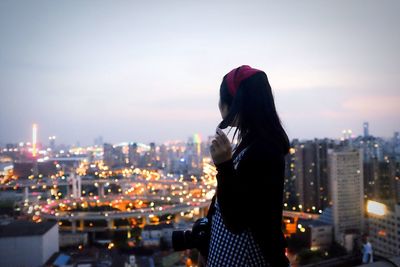 Rear view of woman standing against illuminated cityscape