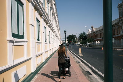 Rear view of woman walking on road amidst buildings in city