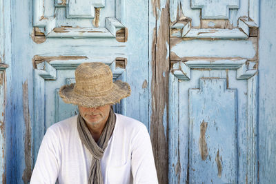 Man with hat and scarf in front of wooden door