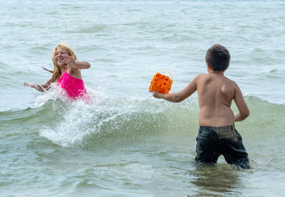 Two cousins chase and splash each other as they play in the waves in lake michigan