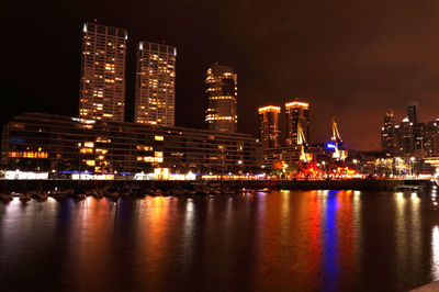 Illuminated buildings by river against sky at night