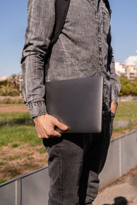 Side view of crop unrecognizable male with hand in pocket holding netbook for working outdoors
