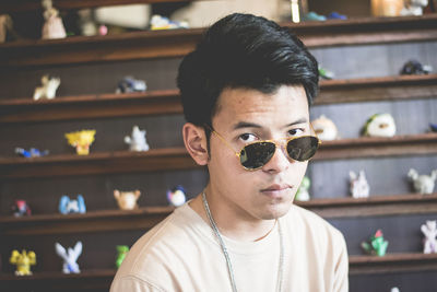 Portrait of young man wearing sunglasses against shelf 