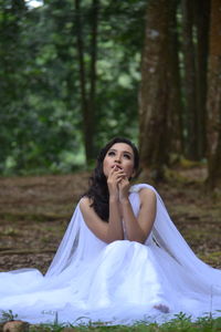 Beautiful bride looking up while sitting on field