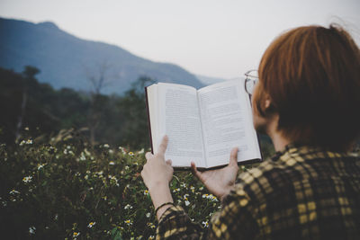 Rear view of woman reading book against mountains