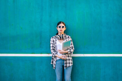 Portrait of young woman standing against blue wall