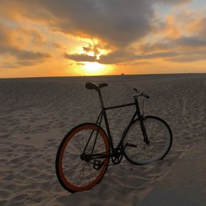 Bicycle on beach against sky during sunset