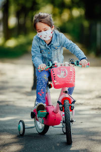 Cute girl wearing mask riding bicycle on road