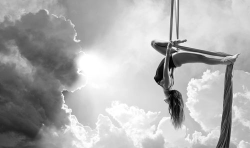 Low angle view of dancer hanging on textile while dancing against cloudy sky