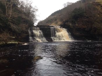 Scenic view of waterfall in forest against clear sky