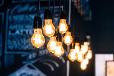 Close-up of illuminated light bulb hanging from ceiling