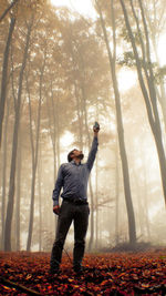 Full length of man standing with arms raised in forest during autumn