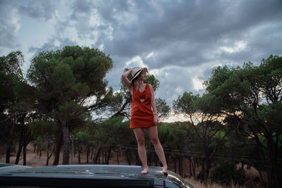 Travel concept - woman standing on the roof of a camper van in the forest at sunset