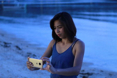 Young woman photographing through mobile phone at beach