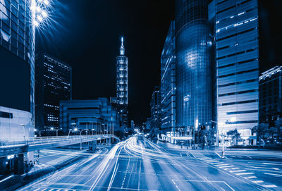 Light trails on city street amidst buildings at night