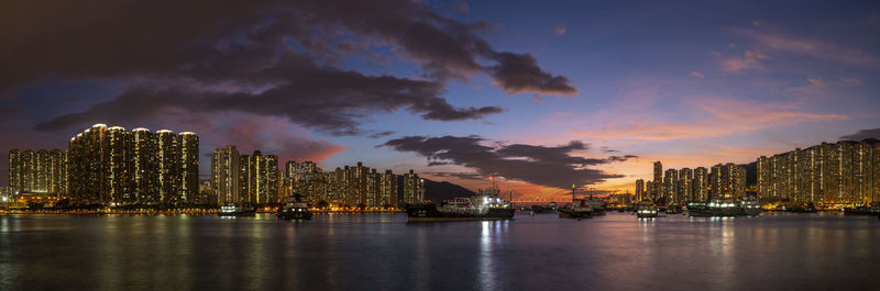 Illuminated buildings by river against sky at night