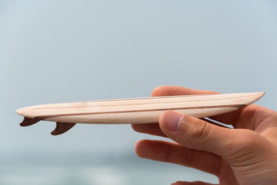 Cropped hand of person holding small surfboard against sky