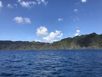 Scenic view of sea by mountain against sky